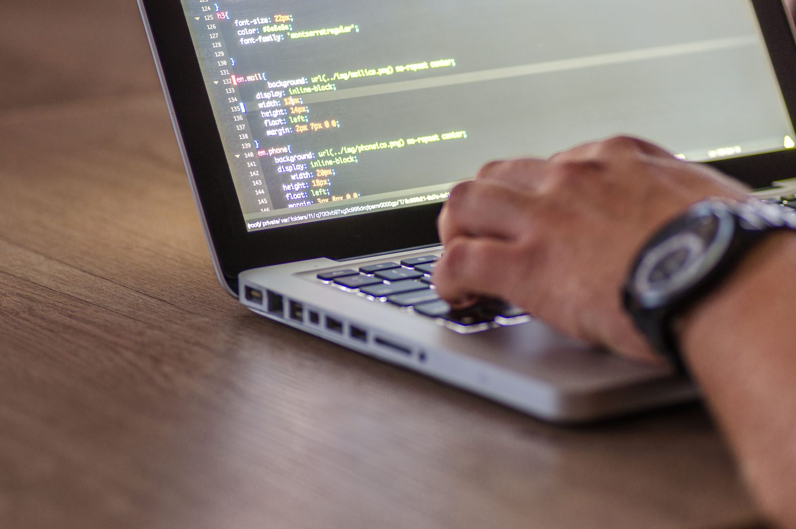 A hand typing on a laptop, the screen showing CSS rules. Every change here becomes a commit message that has to say what it did.
