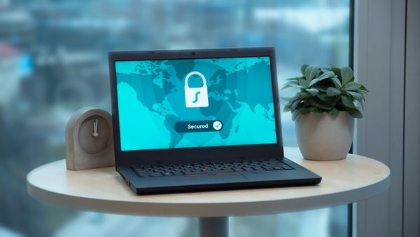 Un ordinateur portable affichant une icone de cadenas et une coche Secured sur une carte du monde. La connexion resistante au phishing vise a verrouiller l'acces au compte sur le vrai appareil.
