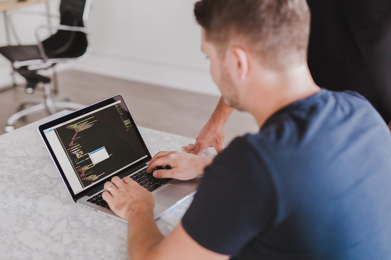 Eine Person arbeitet an einem Laptop, der in einem Editor bunten Quellcode anzeigt