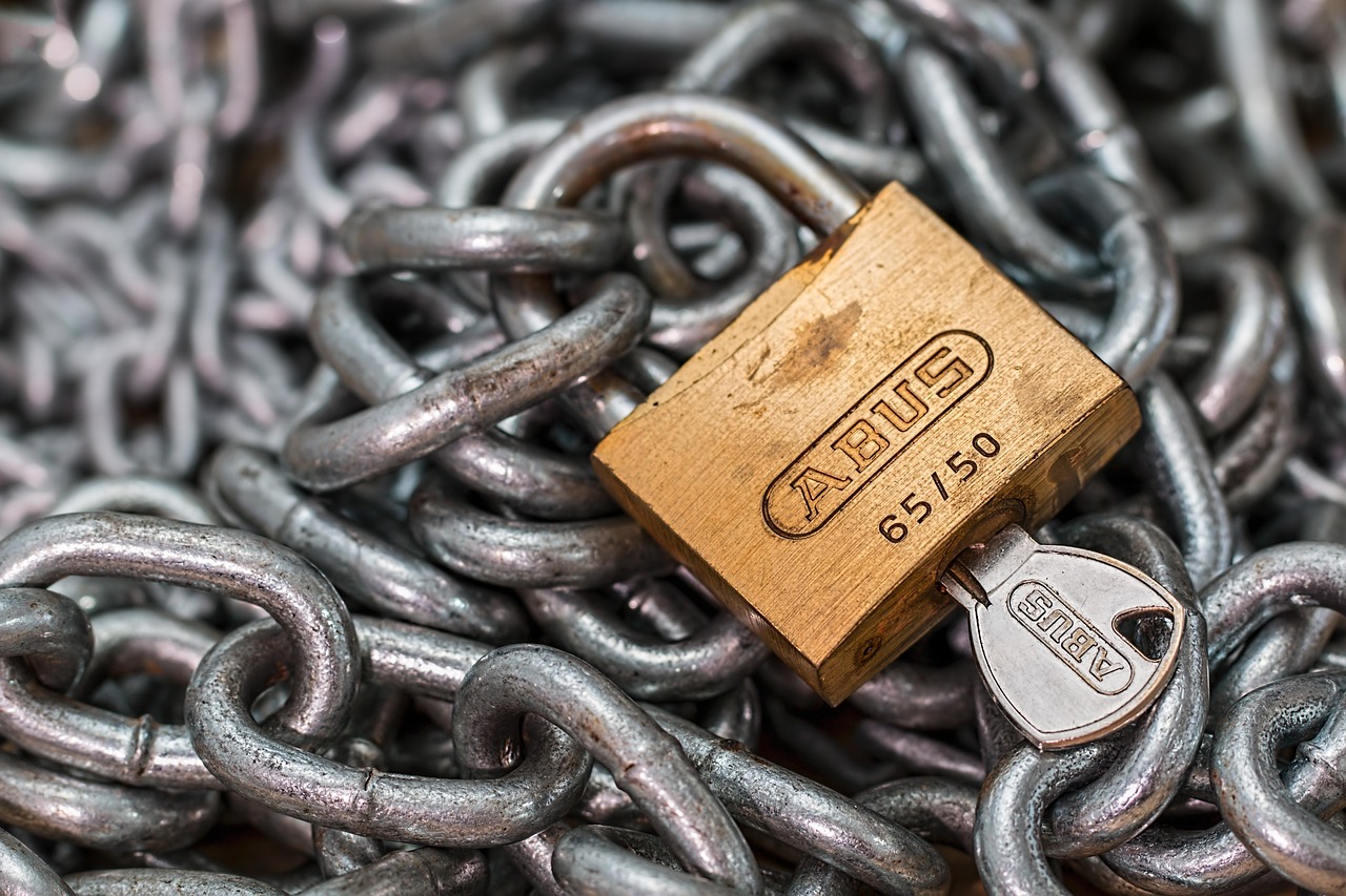 A brass padlock and its key resting on a pile of steel chains.