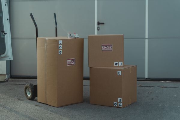 Scatole di cartone con la scritta FRAGILE su un carrello, all'esterno