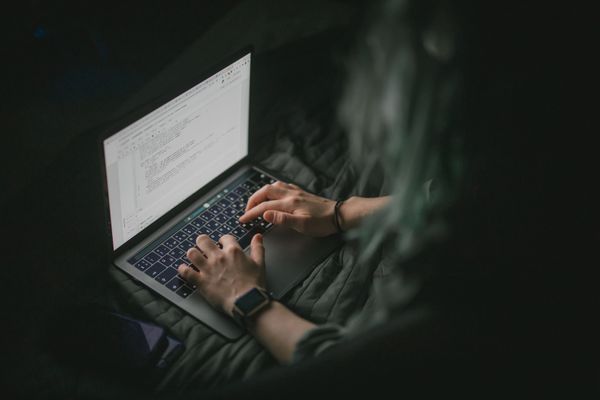 A person's hands typing on a laptop showing code, in a dark room